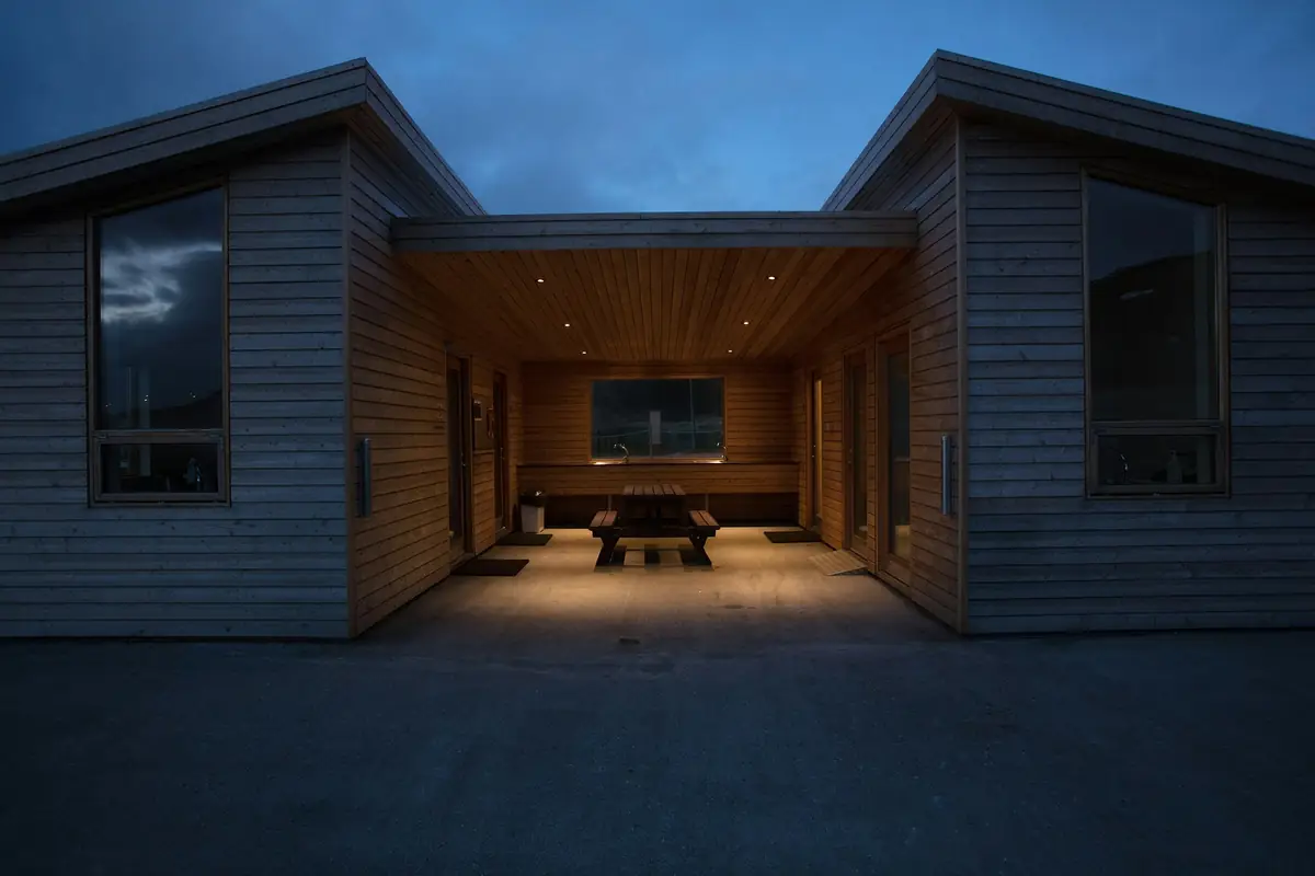 Maison à bardage bois sombre au crépuscule, grande baie vitrée éclairée sur une cour
